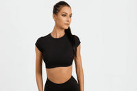 Femme portant un crop top sport noir à manches courtes, taille haute, style élégant et ajusté.