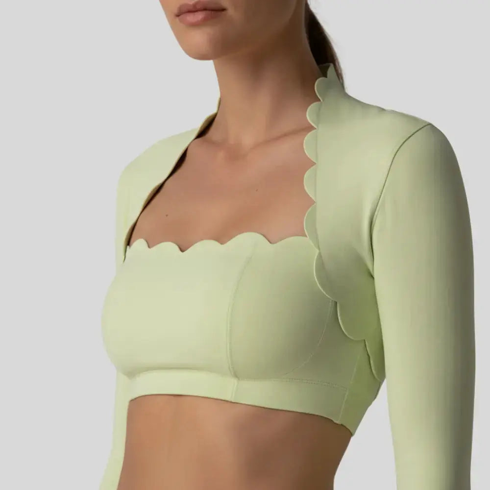 Gros plan sur le top brassière à festons Aura vert FYNESS, mettant en avant la découpe ondulée du col carré et la qualité de la matière sculptante pour une silhouette féminine et assurée.