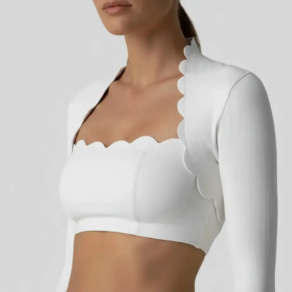 Ce vêtement blanc présente une conception structurée composée d'un bandeau et d'un boléro assorti, tous deux caractérisés par des bordures festonnées distinctives. La matière mate et la coupe ajustée sont mises en valeur par un éclairage de studio uniforme sur un fond gris neutre.